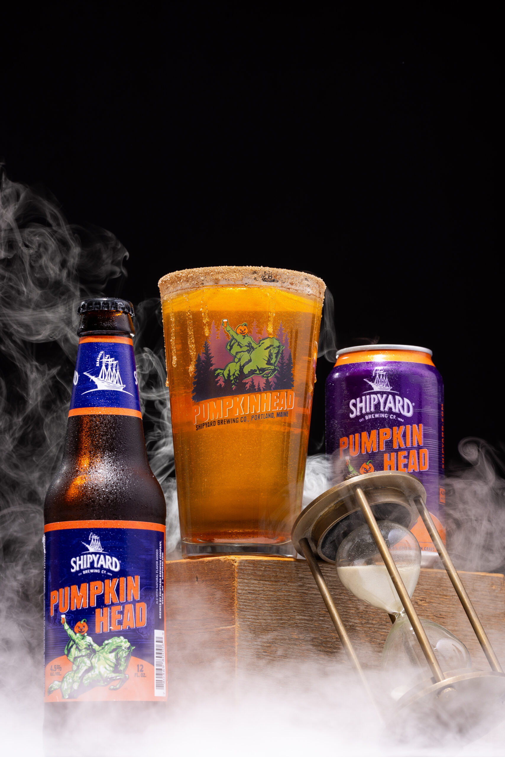 Bottle and glass of Shipyard Pumpkin Head beer on a wooden surface with a dark background and smoky fog